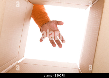 Vue de l'intérieur de boîte en carton avec une main essayant d'atteindre le contenu (selective focus) Banque D'Images