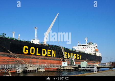 Camion-citerne de carburant énergie dorée amarré amarré au quai du terminal maritime montrant la manutention des boyaux d'huile pour le déchargement grue Banque D'Images