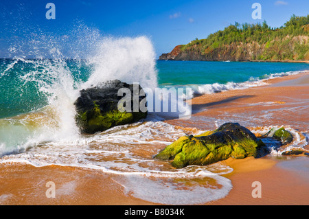 Surf se brisant sur des roches de lave à Kauapea Beach plage secrète Phare Kilauea visible île de Kauai Hawaii Banque D'Images