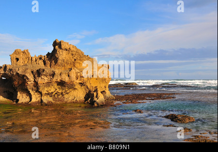 Le soleil du soir met en lumière un affleurement rocheux, se reflétant dans la mer, à Kenton-on-Sea, Afrique du Sud Banque D'Images