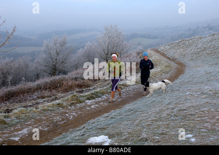 Deux jeunes femmes avec leurs chiens sont vus courir dans les collines de Malvern Worcestershire England Royaume-Uni Europe Banque D'Images