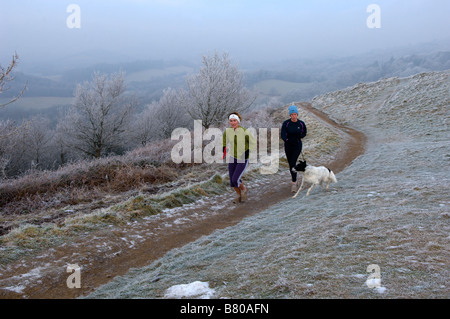 Deux jeunes femmes avec leurs chiens sont vus courir dans les collines de Malvern Worcestershire England Royaume-Uni Europe Banque D'Images