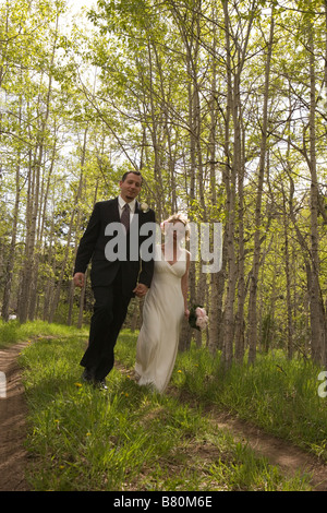 Bride and Groom walking through forest holding hands Banque D'Images