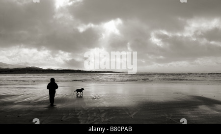 Un homme à pied son chien sur une plage de l'Oregon avec son chien au coucher du soleil. Lincoln City, Oregon, USA. Banque D'Images