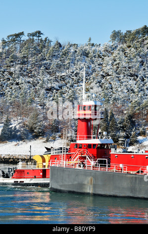 Scène d'hiver avec pittoresque tugboat pushing barge dans l'eau au large du cap Cod littoral avec des arbres couverts de neige fraîchement tombée Banque D'Images