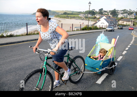 Les pédales d'une mère avec sa fille en montée en remorque derrière sur le front de mer à Falmouth, Royaume-Uni Banque D'Images