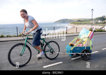 Les pédales d'une mère avec sa fille en montée en remorque derrière sur le front de mer à Falmouth, Royaume-Uni Banque D'Images