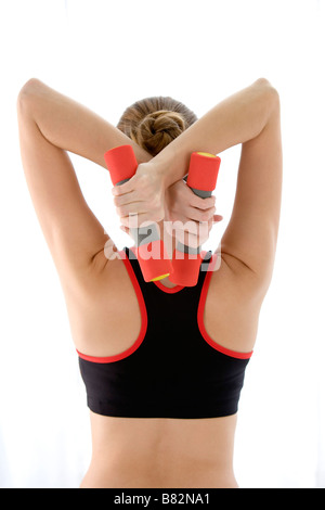 Young woman holding dumbbells derrière la tête vue arrière Banque D'Images