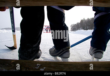 Deux mecs assis sur un banc avec des bâtons de hockey et des patins à l'arrière terrain objectif Banque D'Images