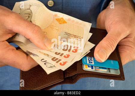 Homme tenant et prenant des billets de banque anglais de l'argent un portefeuille avec des cartes bancaires gros plan Banque D'Images