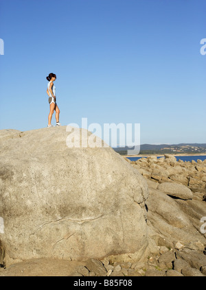 Une femme sur un jog climes au sommet d'un rocher et saute de joie Banque D'Images