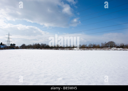 Pylônes électriques dans un champ couvert de neige contre un ciel bleu Banque D'Images