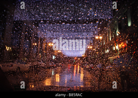 Feuilles de lumières de Noël blanc enfilés sur une rue de ville sur une nuit pluvieuse Banque D'Images