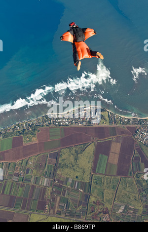 Parachutiste au sein d'une wingsuit orange est en survolant les nuages le long des plages de la Côte-Nord Oahu, Hawaï, Amérique latine. Banque D'Images