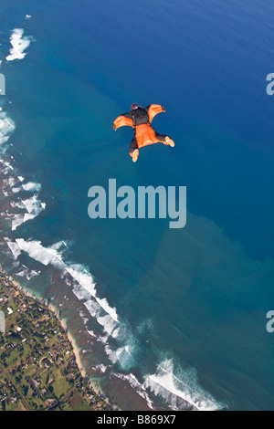 Parachutiste au sein d'une wingsuit orange est en survolant les nuages le long des plages de la Côte-Nord Oahu, Hawaï, Amérique latine. Banque D'Images