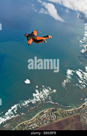 Parachutiste au sein d'une wingsuit orange est en survolant les nuages le long des plages de la Côte-Nord Oahu, Hawaï, Amérique latine. Banque D'Images