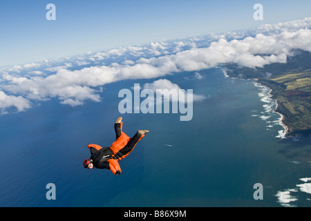 Parachutiste au sein d'une wingsuit orange est en survolant les nuages le long des plages de la Côte-Nord Oahu, Hawaï, Amérique latine. Banque D'Images