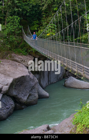 L'Amérique centrale, le Costa Rica. Un homme marche sur la rivière Pacuare sur un pont suspendu. Banque D'Images