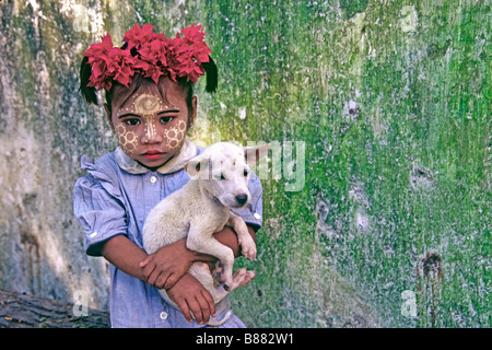 Petite fille avec thanaka sur visage, tenant un chiot ; Amarapura, Mandalay, Myanmar (Birmanie) Banque D'Images