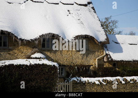 Maison en pierres avec son toit recouvert de neige avec des glaçons pendant de celui-ci. Banque D'Images