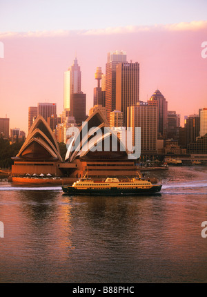 Location de bateau avec les passagers traversant le Port de Sydney en vertu de l'Opera House et sur les toits de la ville à l'aube Banque D'Images