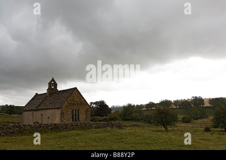 Dans la pluie sous ciel gris derrière un mur en pierre sèche Cotswold - st oswald's Church Windrush Valley Cotswold Hills Banque D'Images
