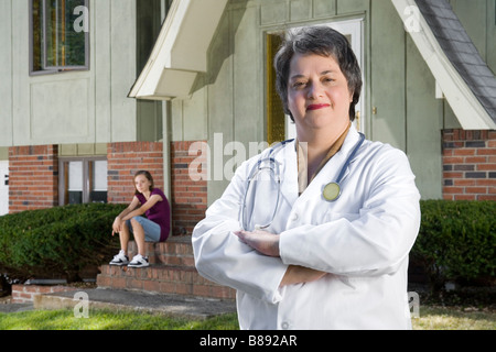 Femme médecin d'âge moyen, devant une maison avec un adolescent assis derrière elle sur une étape. Banque D'Images