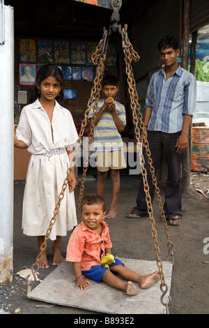 Pose de l'enfant sur une grande échelle de pesage à un décrochage du marché de rue, avec la famille. Hazira, Surat, Gujarat. L'Inde. Banque D'Images