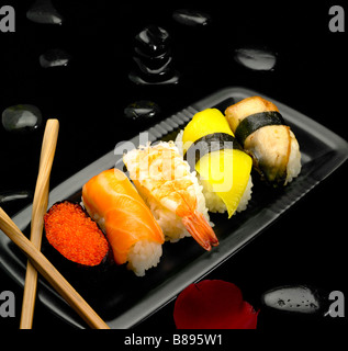 Assortiment de sushi sur plaque de cailloux noirs sur fond noir Banque D'Images