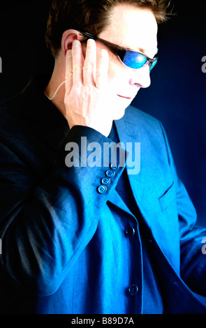 Portrait d'un homme à l'écoute jusqu'à l'écouteur, portant des lunettes de soleil. À la recherche vers une lumière bleue. Banque D'Images