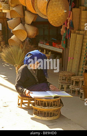 Vieille Femme à la lecture livre en face du magasin qui vend des produits en bambou, Luang Prabang, Laos Banque D'Images