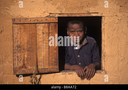 Un garçon Betsileo dans la fenêtre de sa maison en brique d'Adobe ou de boue dans le centre de Madagascar, près d'Ambalavao, Madagascar Banque D'Images
