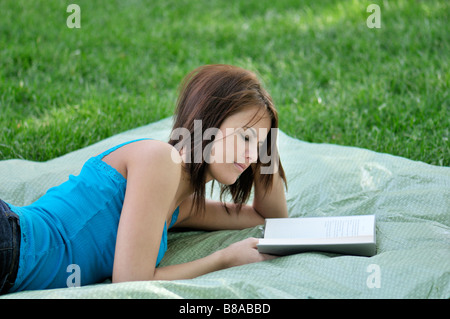 Une jolie fille se trouve sur une couverture à l'extérieur et lit un livre. USA. Banque D'Images