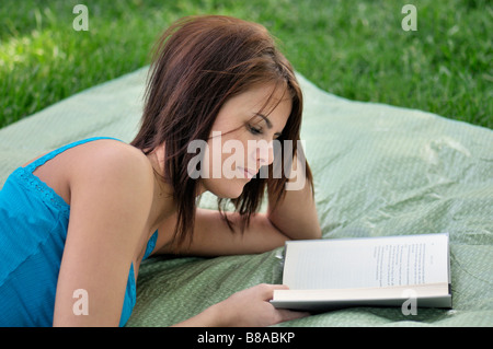 Une jolie brune, caucasian girl se trouve sur une couverture à l'extérieur et lit un livre. USA. Banque D'Images