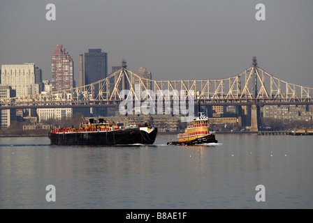 Un remorqueur remorque une barge dans l'East River à New York Banque D'Images