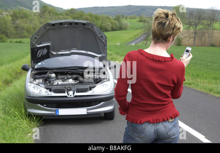 Femme avec sa voiture en panne dans la campagne à l'aide de son téléphone portable pour appeler à l'aide Banque D'Images