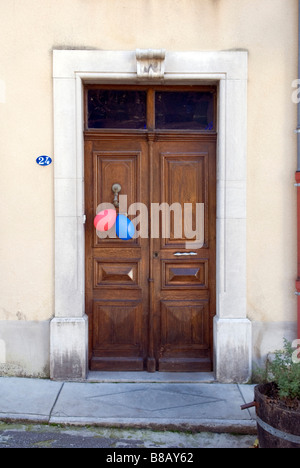 Des ballons rouges et bleus, ce qui suggère une fête d'enfants, se suspendre à une vieille porte dans un village français Banque D'Images