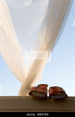 Une paire de dames sandales rouge perché sur un rebord de fenêtre avec des rideaux filet à l'arrière Banque D'Images