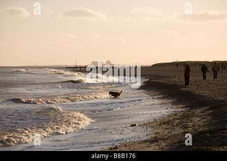 Les promeneurs sur la plage de Southwold hiver en soirée après-midi au soleil avec la centrale nucléaire de Sizewell à distance Banque D'Images