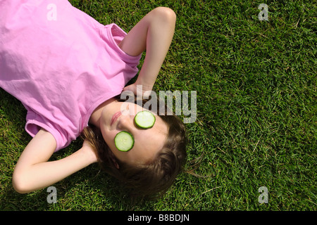 Jeune fille portant des tranches de concombre sur les yeux de l'herbe Banque D'Images