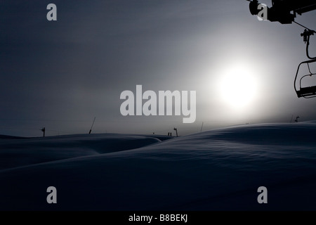 Ascenseur de chaise avec soleil derrière les pentes couvertes de neige sur les Alpes Françaises Saises Banque D'Images