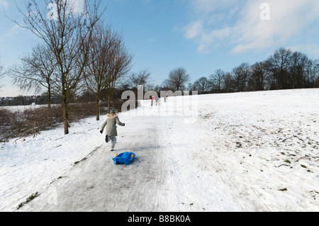 Enfant tirant un traîneau en montée sur Hampstead Heath couvert de neige, Londres, Angleterre, Royaume-Uni Banque D'Images
