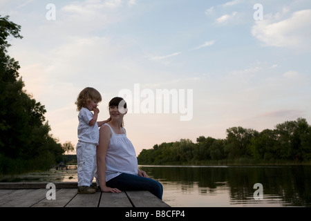 Mère et fille enceinte Sitting on Jetty en soir Banque D'Images