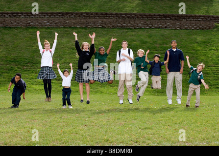 Les étudiants d'une salle de 000 à 12 l'école de catégorie sauter de joie dans un champ vert. Banque D'Images