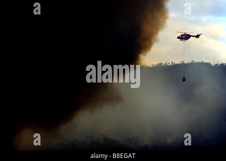 Un hélicoptère avec godet de mousson la lutte contre un feu de brousse en Nouvelle Zélande Banque D'Images