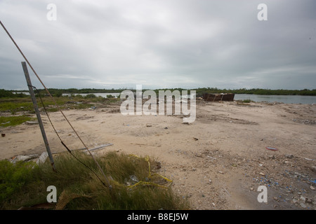 Lot vide avec les lignes électriques et corbeille sur le côté du lagon d'Ambergris Caye au Belize près de coucher du soleil et un ciel couvert. Banque D'Images