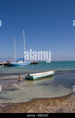 Un petit bateau est lié à un jeu dans les bas-fonds avec des voiliers à l'horizon sous un soleil d'après-midi chaud : Ambergris Caye, Belize Banque D'Images