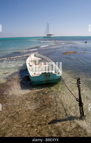 Un petit bateau est lié à un jeu dans les bas-fonds avec des voiliers à l'horizon sous un soleil d'après-midi chaud : Ambergris Caye, Belize Banque D'Images