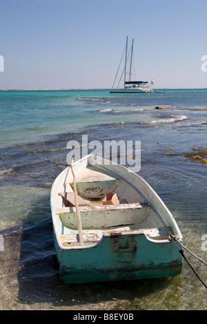 Un petit bateau est lié à un jeu dans les bas-fonds avec des voiliers à l'horizon sous un soleil d'après-midi chaud : Ambergris Caye, Belize Banque D'Images