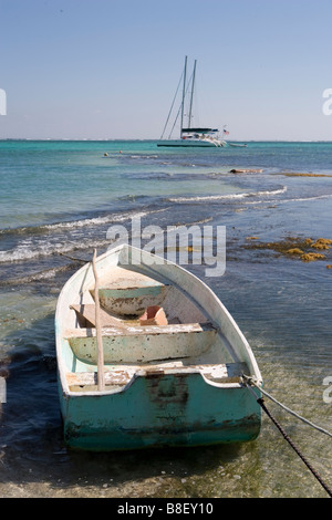 Un petit bateau est lié à un jeu dans les bas-fonds avec des voiliers à l'horizon sous un soleil d'après-midi chaud : Ambergris Caye, Belize Banque D'Images